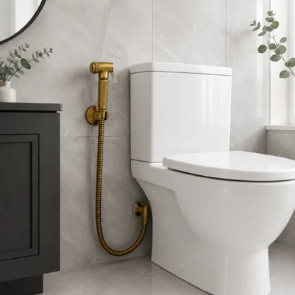 Douchette WC en laiton vieilli installée près d’une toilette blanche