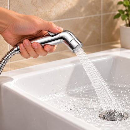 Main tenant une douchette WC chromée inclinée vers un lavabo